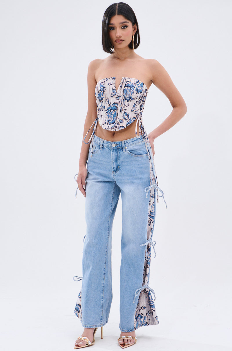 A woman stands confidently in heeled sandals, wearing a floral strapless top and SEASONAL AWAKENING BROCADE PATCH DENIM JEANS with brocade side panels and lace-up details against a plain white background. 8