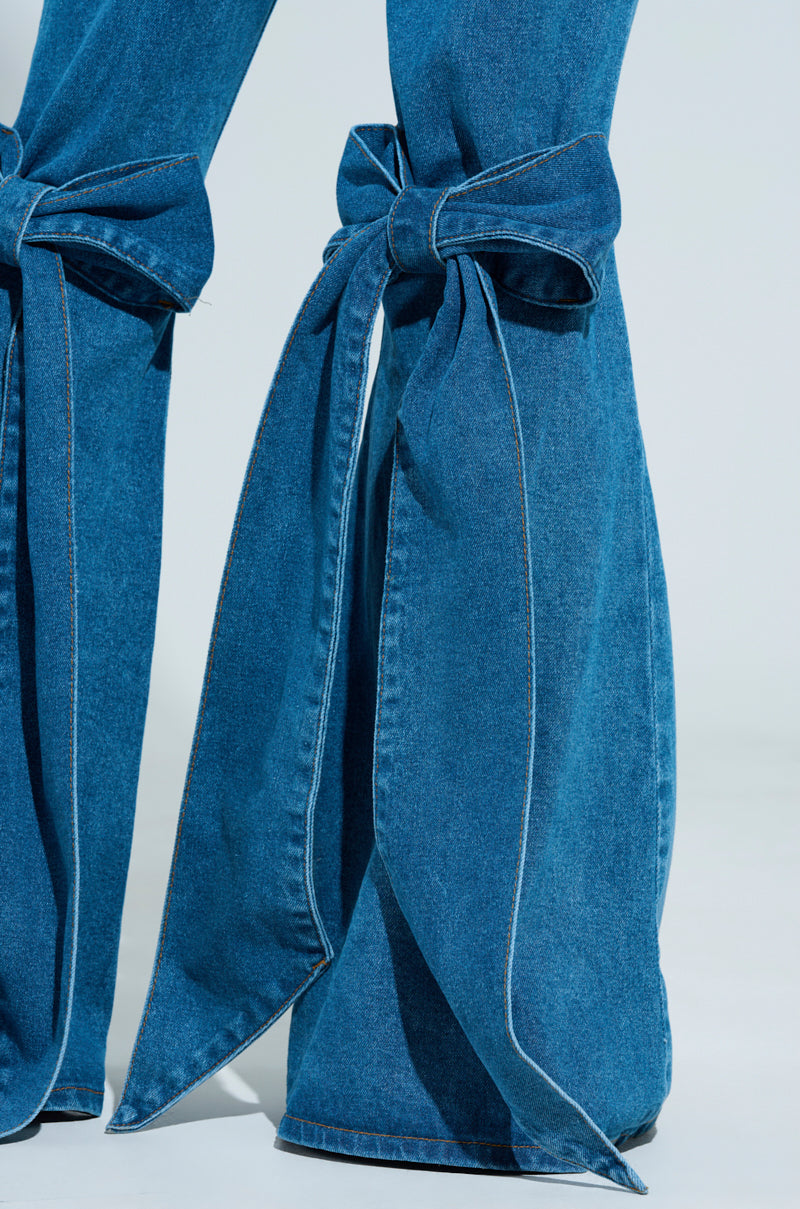 Close-up of ALL TIED UP BOW FLARE JEANS in high-rise blue denim, featuring large decorative bows on the lower legs for a stylish twist on traditional flare jeans against a plain background. 5