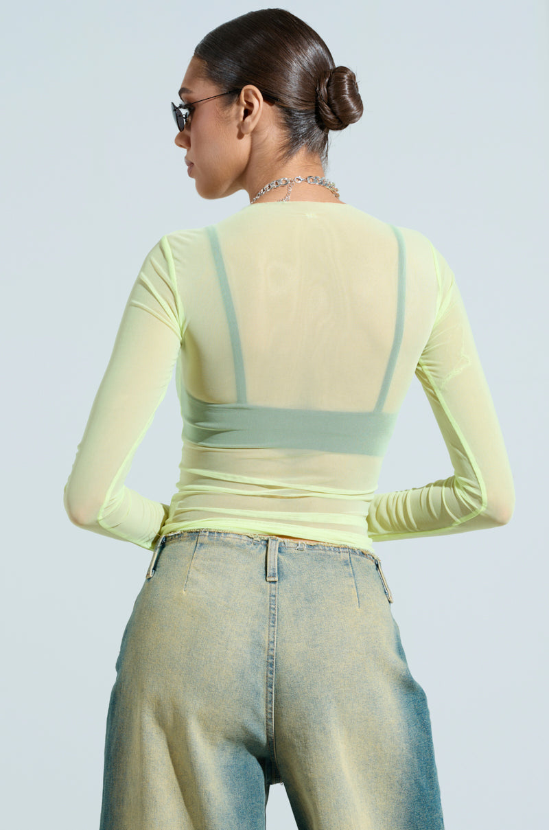 A person with long hair in a neat bun is wearing sunglasses and the PAXTON SEXY DOUBLE LINED MESH LONG SLEEVE TOP, paired with blue jeans. They face away from the camera against a plain background, exuding an effortlessly club-ready vibe.