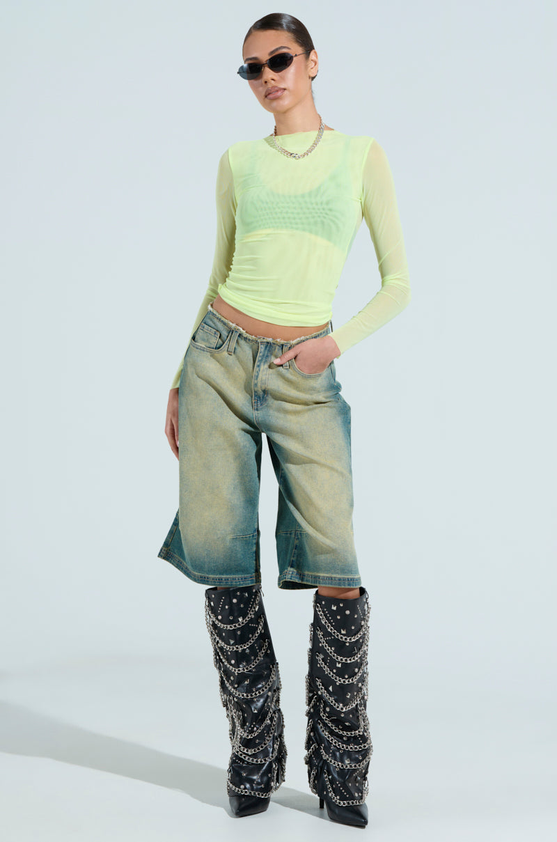 Clad in the PAXTON SEXY DOUBLE LINED MESH LONG SLEEVE TOP, a person wears sunglasses and knee-length denim shorts paired with tall black boots adorned with chains, exuding confidence with a modern, edgy club-ready style.