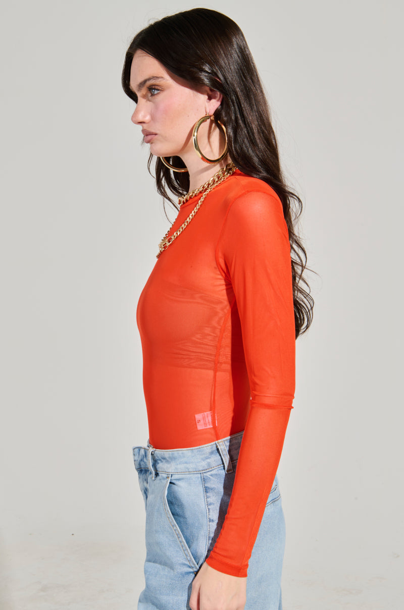 A woman with long dark hair wears the PAXTON Mesh Long Sleeve Crew Neck Bodysuit in a vibrant orange color, paired with light blue jeans. She accessorizes her outfit with large hoop earrings and a chunky gold necklace against a plain light gray background.