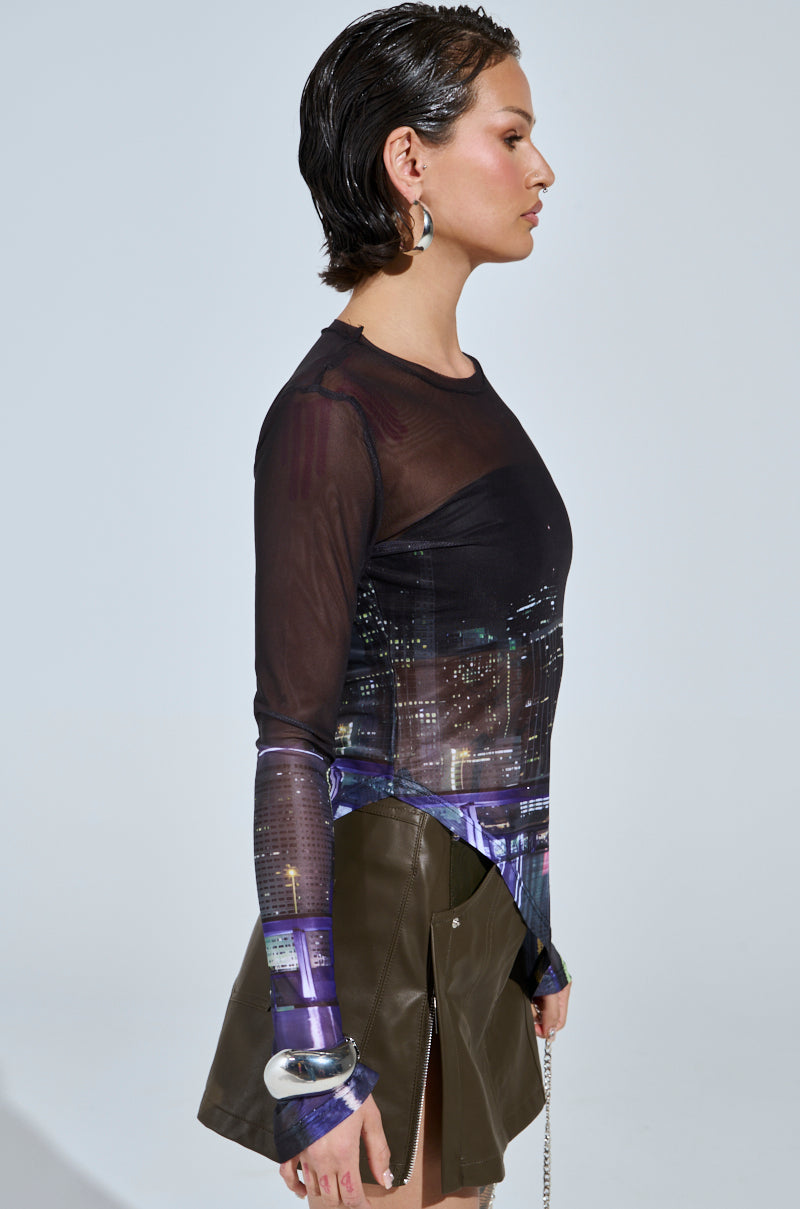 A person sporting slicked-back hair wears the CITY LIFE MESH TOP paired with olive green zippered pants. Hoop earrings and a bracelet complete the look as they pose in profile against a plain backdrop.