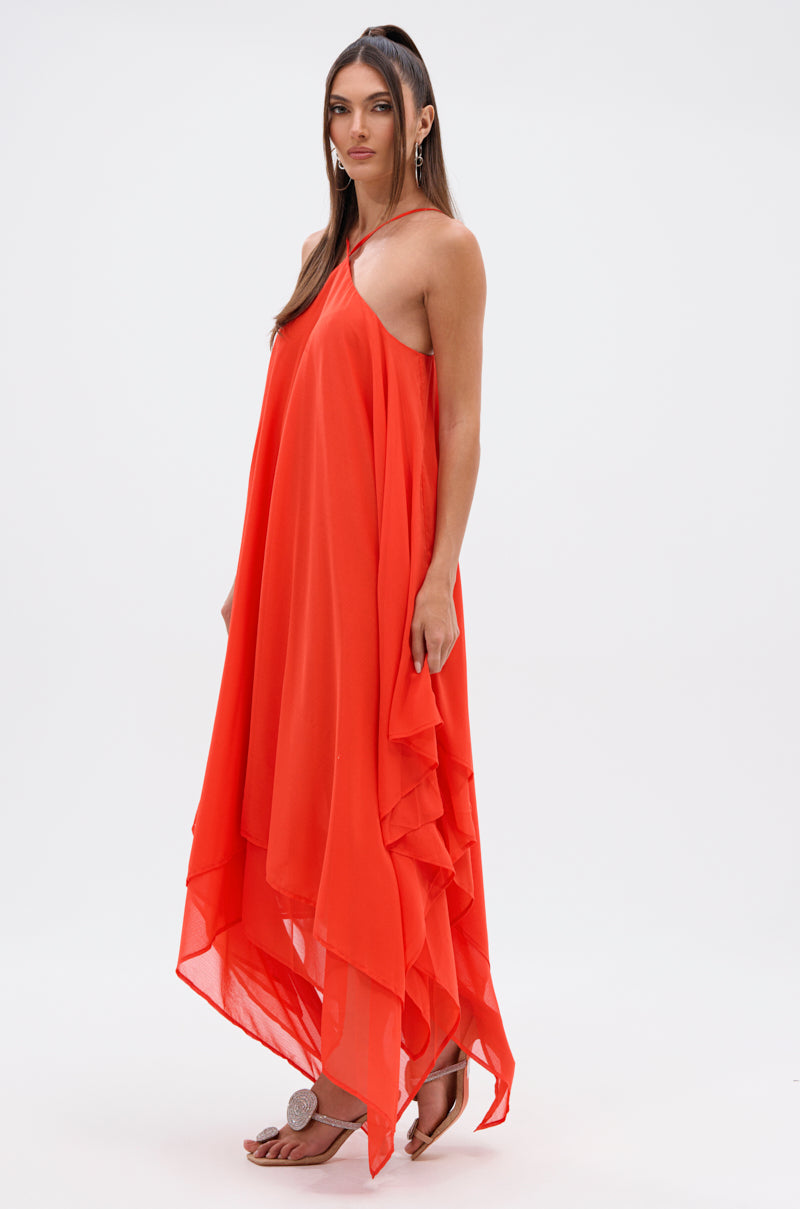 Model wears the RUNAWAY CHIFFON MAXI DRESS in vibrant orange, featuring a halter neckline and asymmetrical hem, styled with tan flat sandals and dangling earrings against a plain white background.