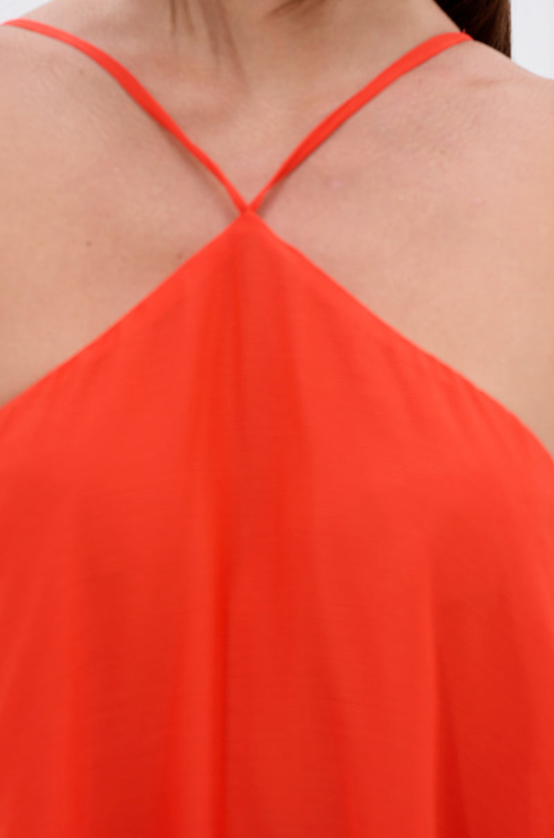 Close-up of a person wearing the RUNAWAY CHIFFON MAXI DRESS, featuring a bright red halter neckline with thin straps crossing at the neck, revealing shoulders and upper chest. The background is blurred.