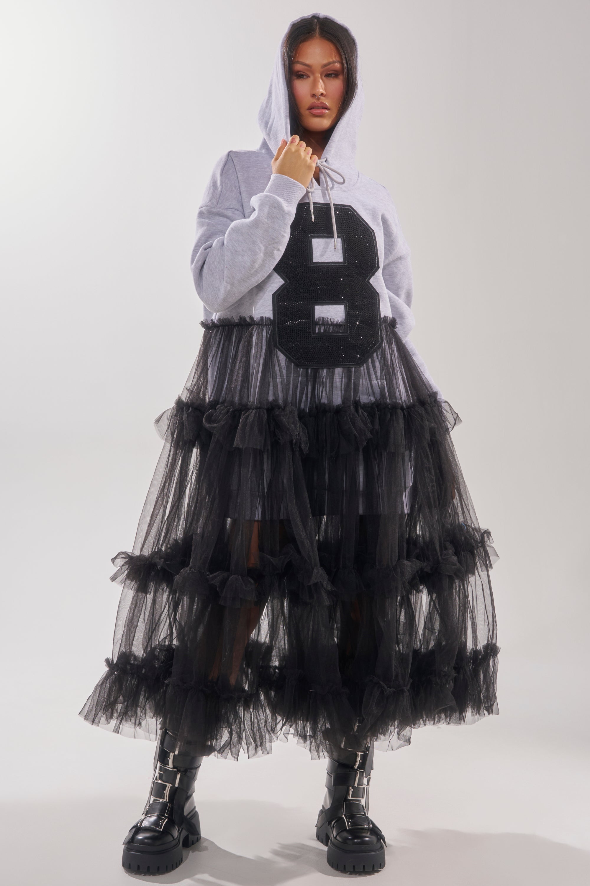 Wearing the DO SOMETHING CRAZY SWEATSHIRT DRESS in gray with a bold black "8," paired with a black ruffle maxi skirt and black buckle boots, someone stands against a plain light background.