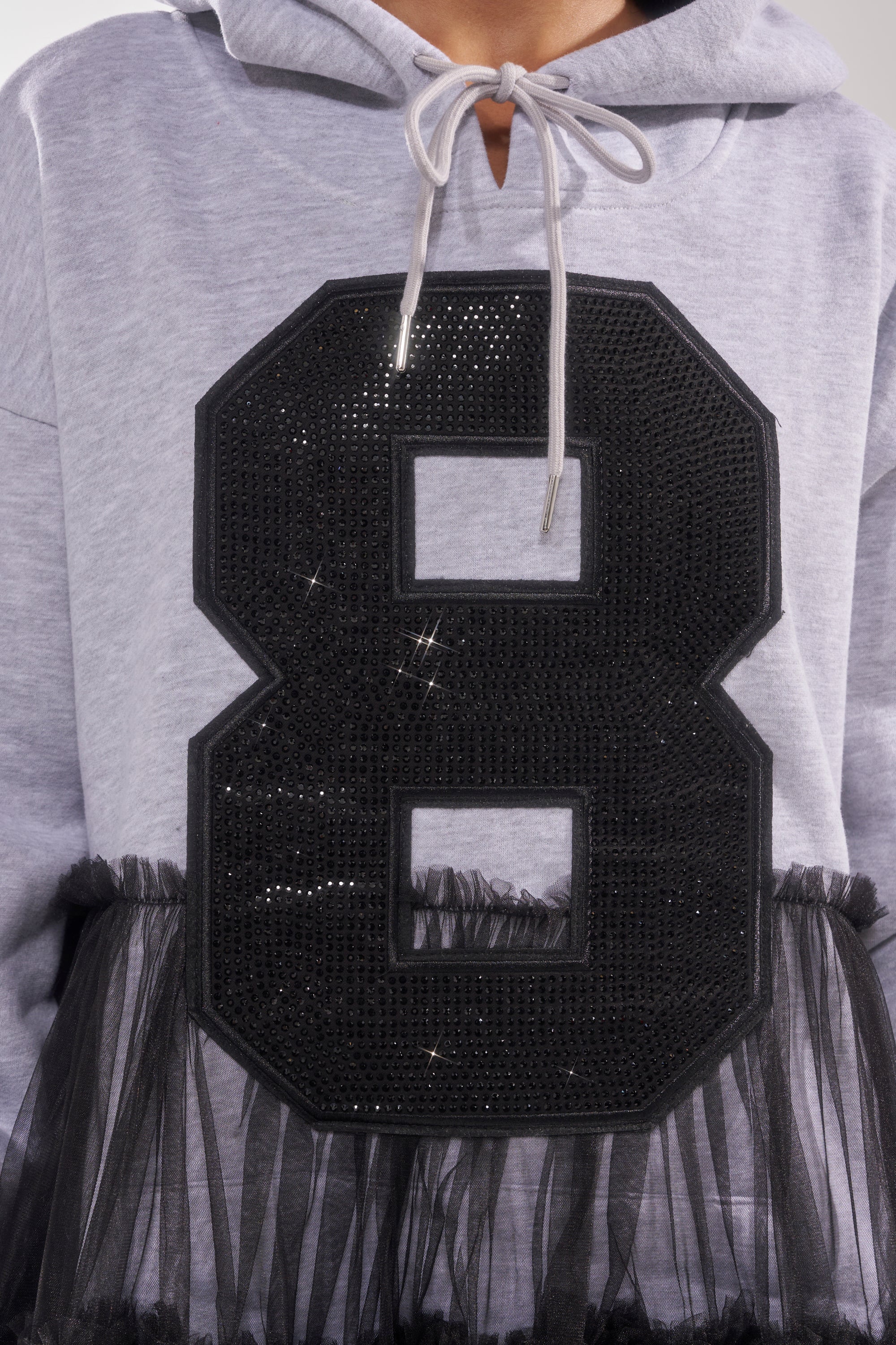 The DO SOMETHING CRAZY SWEATSHIRT DRESS is a light gray, relaxed-fit dress with a bold black sequined number 8 and black tulle trim, drawstrings, and is perfect for pairing with a ruffle maxi skirt.