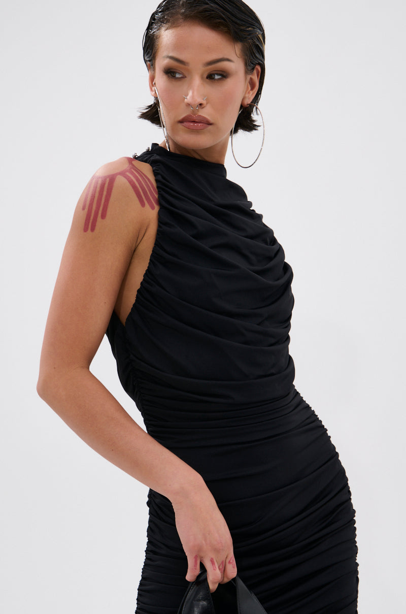 Wearing the BUSINESS IN FRONT PARTY IN BACK MIDI DRESS IN BLACK, a person with short dark hair, large hoop earrings, and a pink abstract shoulder tattoo stands against a plain background, looking slightly down and to the side.