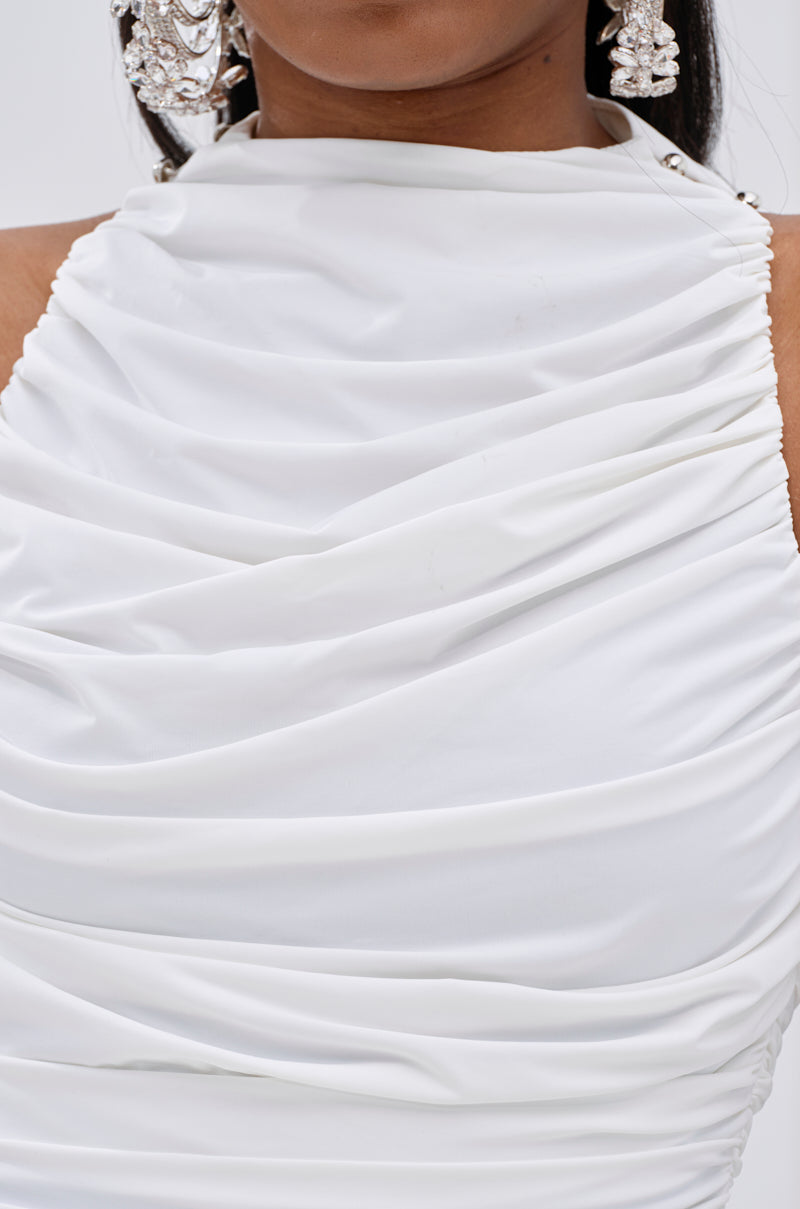 A close-up of a person wearing the BUSINESS IN FRONT PARTY IN BACK MINI DRESS IN WHITE, featuring a curve-hugging fit, sleeveless design, high neckline, silver-tone shoulder buttons, and paired with ornate silver earrings. The image highlights dress details and earrings. 7