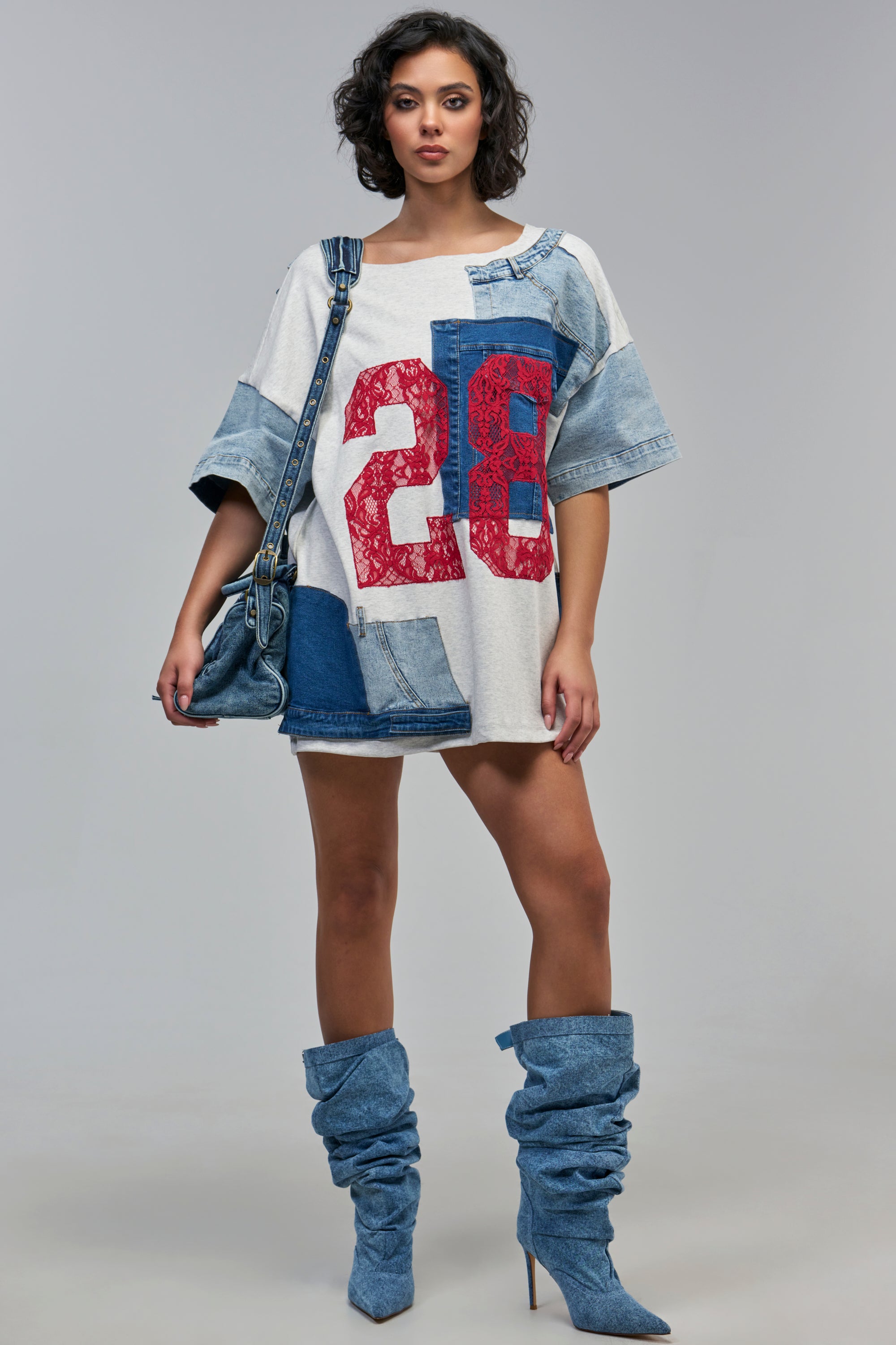 The SIDELINE JERSEY MINI DRESS IN DENIM PATCHWORK is an oversized streetwear style featuring denim patchwork and a large red number graphic, paired with slouchy denim boots.