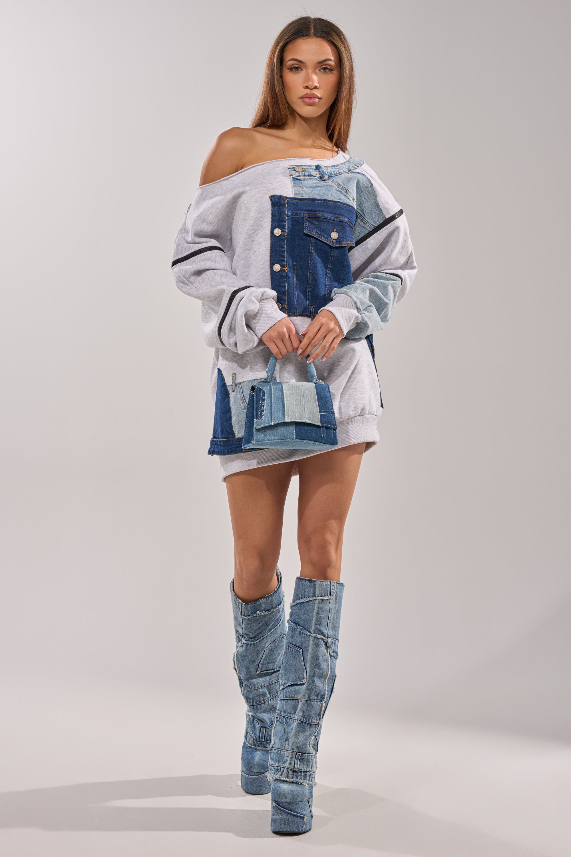 A woman stands confidently in the ADIRA MINI SWEATER DRESS, paired with tall patchwork denim boots and a small denim handbag against a plain light-colored background. 10