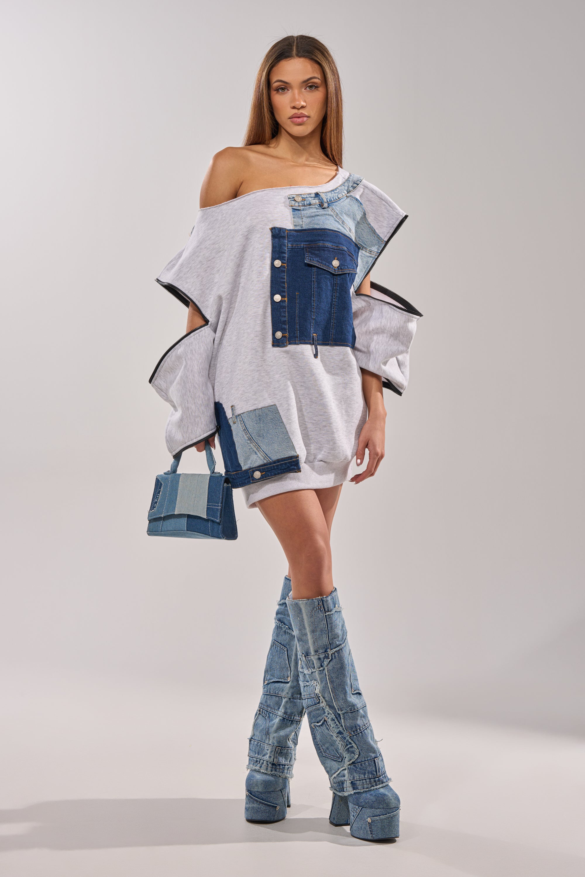 A woman wears the ADIRA MINI SWEATER DRESS, styled with knee-high denim boots and a matching handbag, set against a plain light background. 12