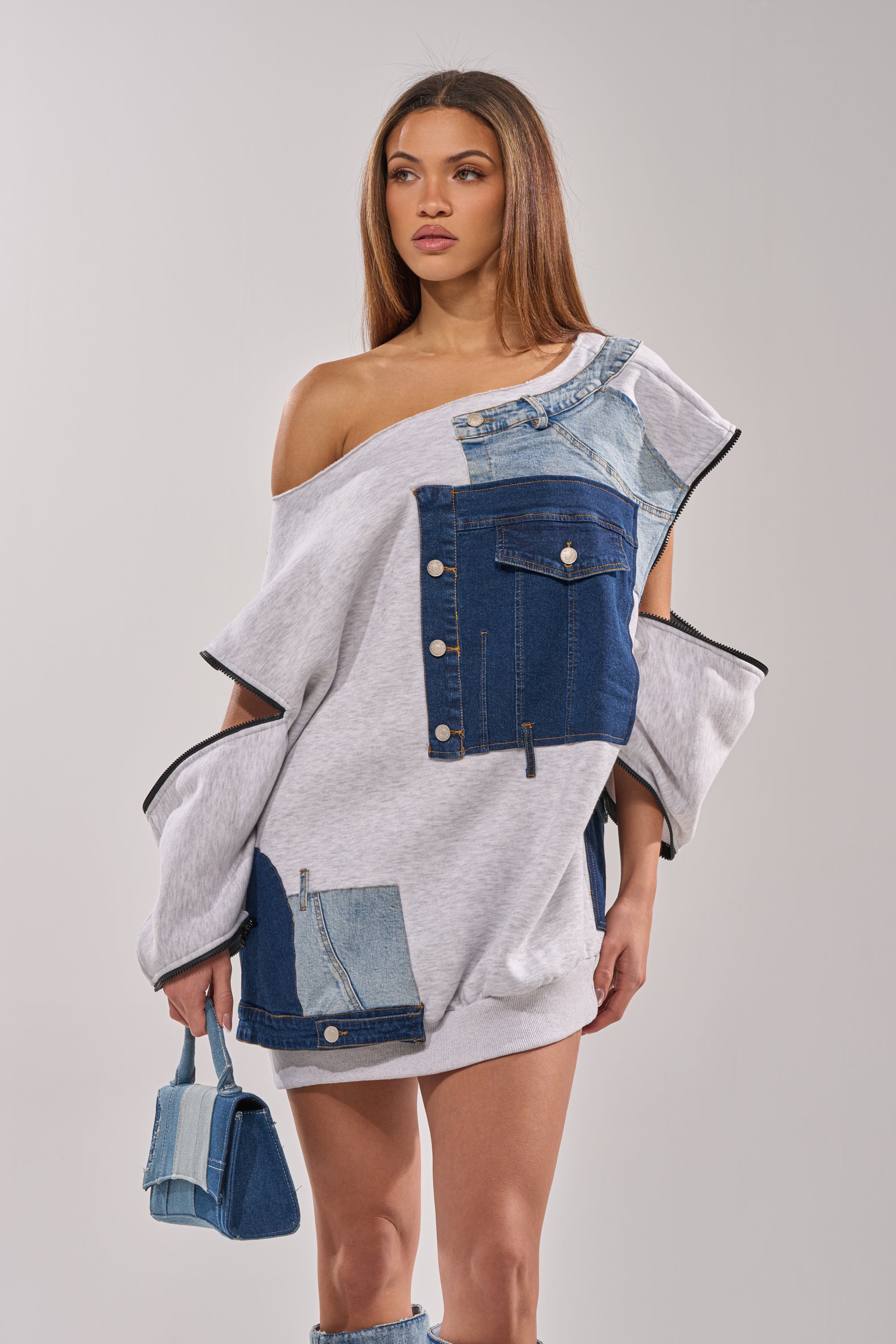 A woman in the ADIRA MINI SWEATER DRESS holds a matching purse as she poses against a simple light background. 5