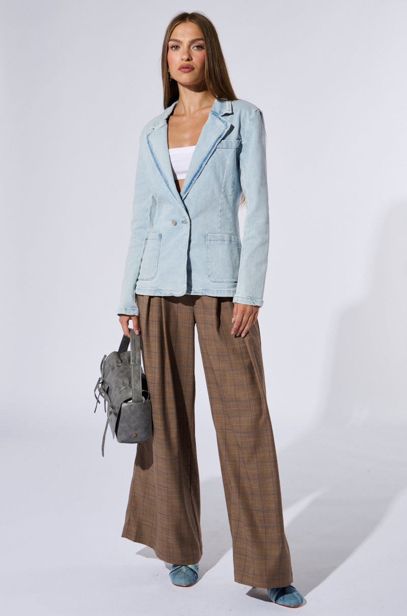 A woman stands against a plain background, showcasing business chic in a light blue **ROBYN DENIM BLAZER** over a white top and relaxed-fit brown plaid wide-leg pants. She holds a gray handbag by her side, wears blue shoes, and has long straight hair with a neutral expression.
