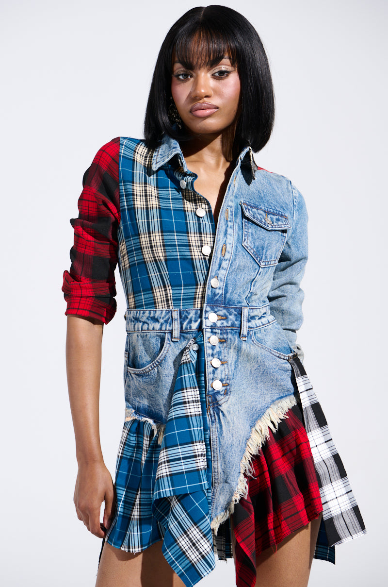 A person wearing an edgy ensemble stands confidently in the PATCHWORK PLAID DENIM MINI DRESS, featuring red and blue elements, frayed edges, and button details. They have shoulder-length black hair and a neutral expression against a plain background.
