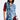 A person wearing an edgy ensemble stands confidently in the PATCHWORK PLAID DENIM MINI DRESS, featuring red and blue elements, frayed edges, and button details. They have shoulder-length black hair and a neutral expression against a plain background.