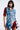 A person wearing an edgy ensemble stands confidently in the PATCHWORK PLAID DENIM MINI DRESS, featuring red and blue elements, frayed edges, and button details. They have shoulder-length black hair and a neutral expression against a plain background.