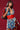 Against a deep red background, a woman showcases her edgy style with the PATCHWORK PLAID DENIM MINI DRESS featuring blue and red patterns. A bright red sash accents the look, teamed with a textured shoulder bag and layered necklaces for the perfect fashion-forward ensemble.