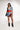 Wearing a PATCHWORK PLAID DENIM MINI DRESS with an asymmetrical hemline, accessorized with short hair, a necklace, and a small handbag. Pointed black boots complete the punk-inspired outfit featuring denim over red and blue plaid.