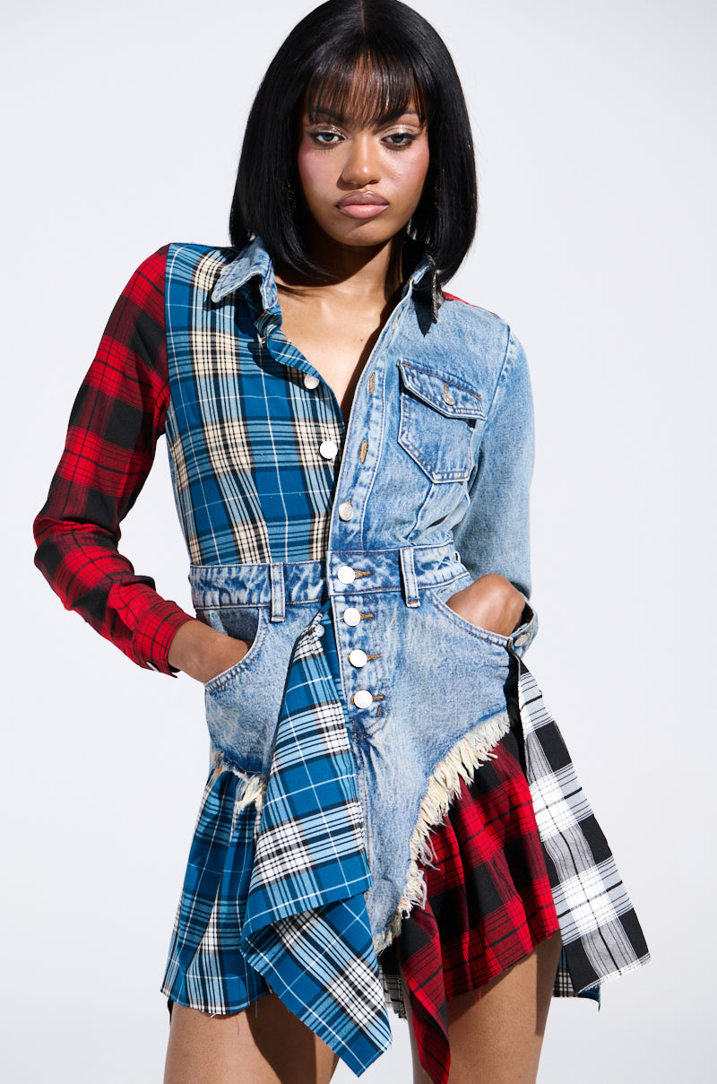 A woman stands confidently in a PATCHWORK PLAID DENIM MINI DRESS. The punk-inspired dress features multicolored plaid sections, a fringed hem, long sleeves, and button details. Her shoulder-length black hair frames her face as she casually keeps her hands in her pockets.