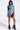 Wearing the PATCHWORK PLAID DENIM MINI DRESS in red and blue with frayed edges, a person exudes confidence. The ensemble is edgy and punk-inspired, paired perfectly with black fringed ankle boots against a plain white background.