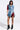 Wearing a PATCHWORK PLAID DENIM MINI DRESS with blue and red tones, styled with medium-length hair and black fringe ankle boots, the person presents a punk-inspired look against a white backdrop.
