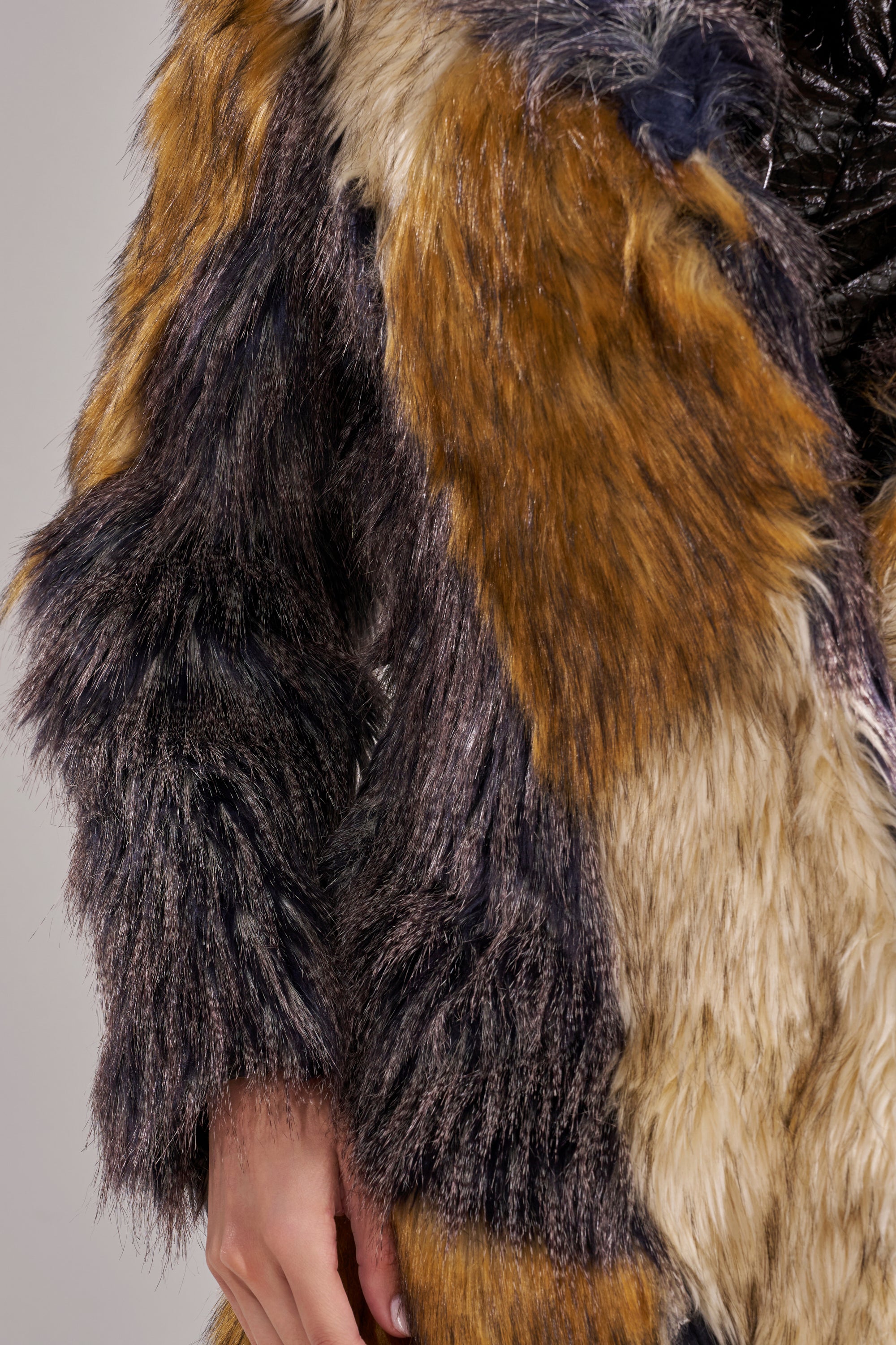 A close-up of a hand and arm wearing the NOTRE DAME FAUX FUR COAT, featuring a bold multicolored patchwork design in brown, black, and cream—perfect for luxury street style.