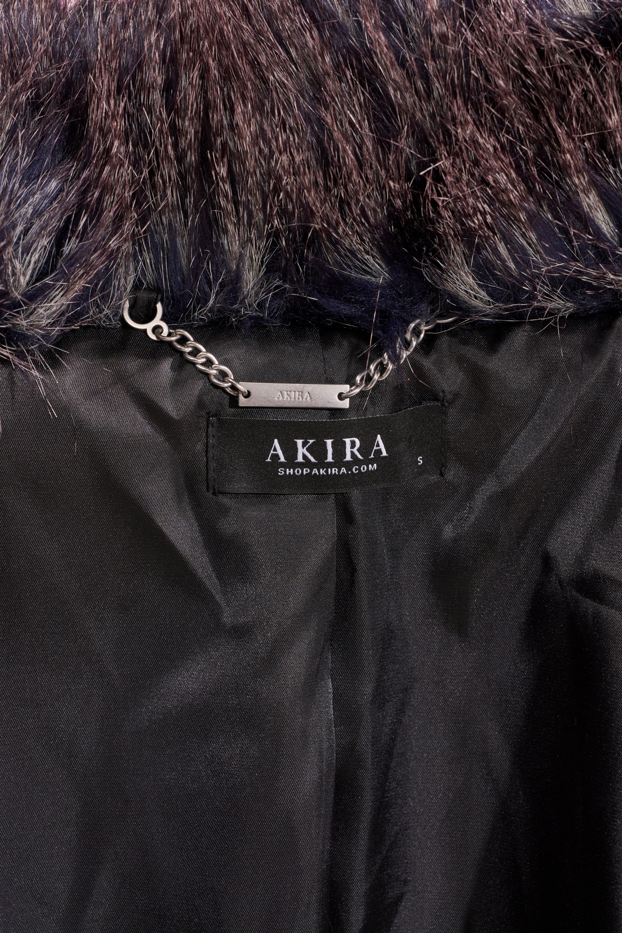 Close-up of the inside collar of the NOTRE DAME FAUX FUR COAT, showing a patchwork design, metal hanging chain, and black "AKIRA SHOPAKIRA.COM" size S label—ideal for elevating your luxury street style.