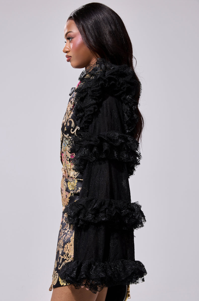 A woman in profile models the LORY PRINTED BLAZER DRESS, featuring sheer ruffled sleeves and gold scrollwork, against a plain light background.