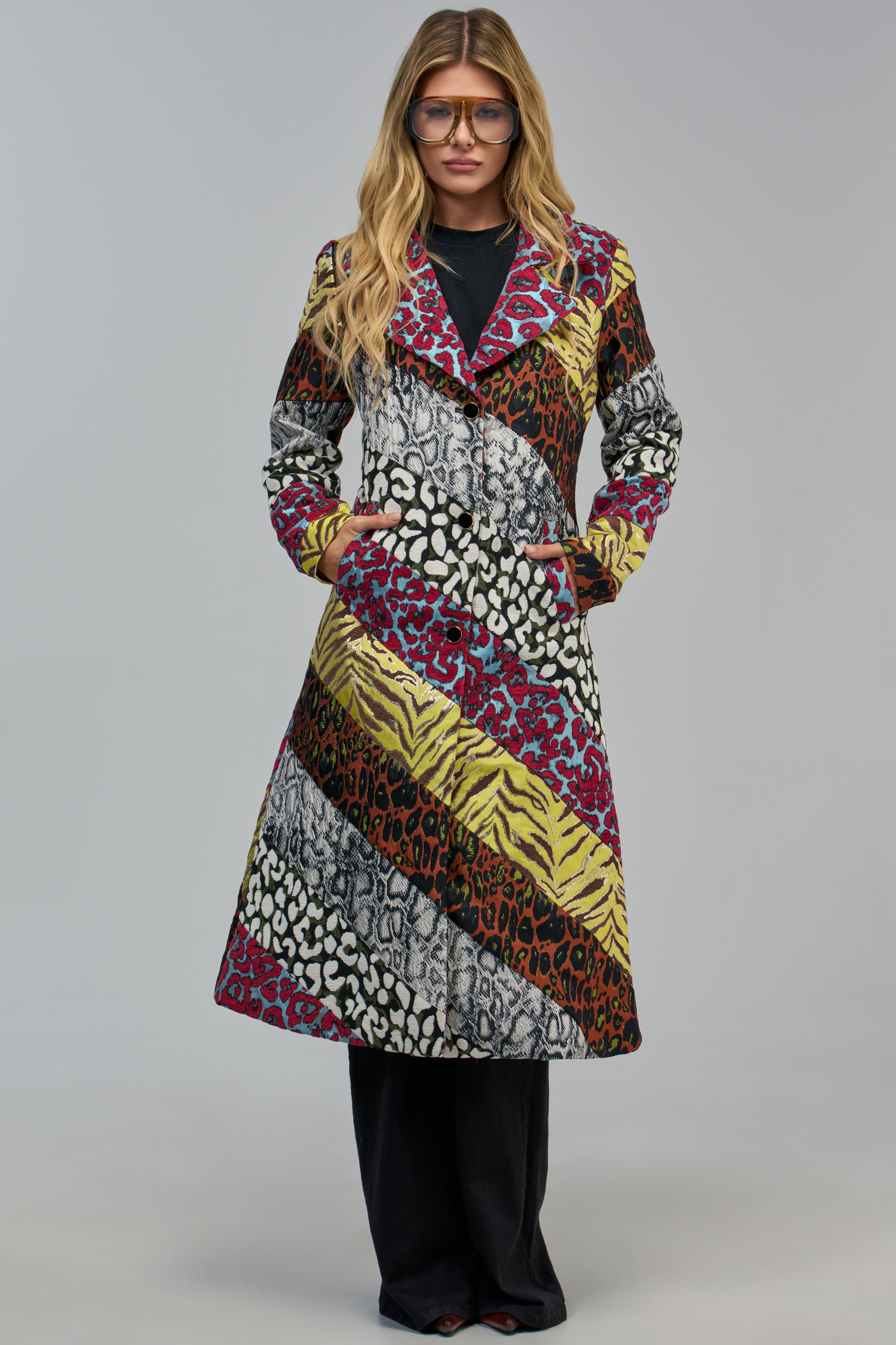 A person wears the HOW I WANT IT PATCHWORK TRENCH, a statement coat featuring diagonal patchwork panels of colorful animal prints.