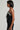 A woman with short dark hair is standing in profile, wearing the luxurious asymmetrical pearl bodysuit. This elegant outfit perfectly complements her style, set against a plain background.