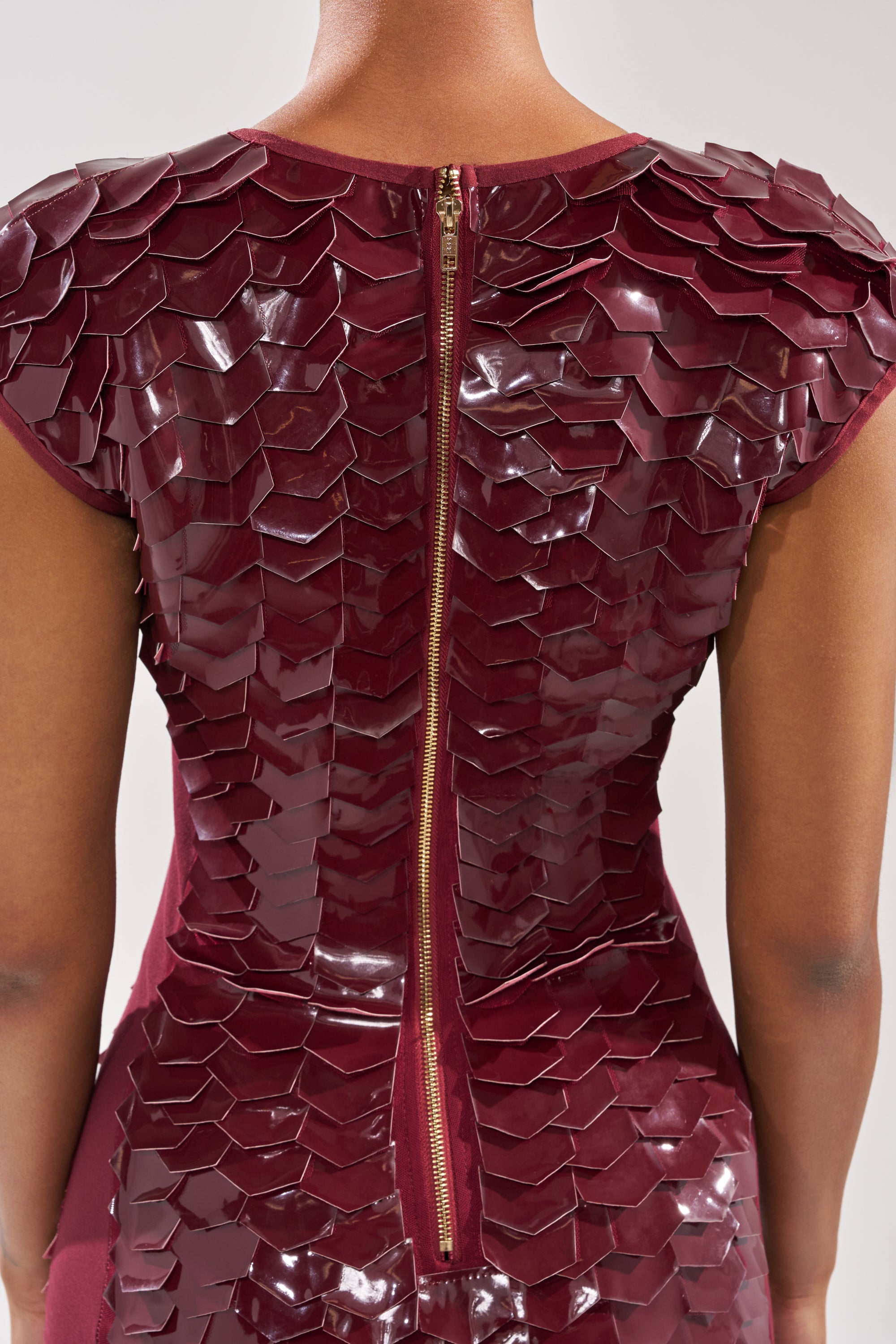 A close-up of a person’s back wearing the CRAZY IN LOVE SCALE MINI DRESS, with burgundy scale-like details and an exposed gold center zipper.