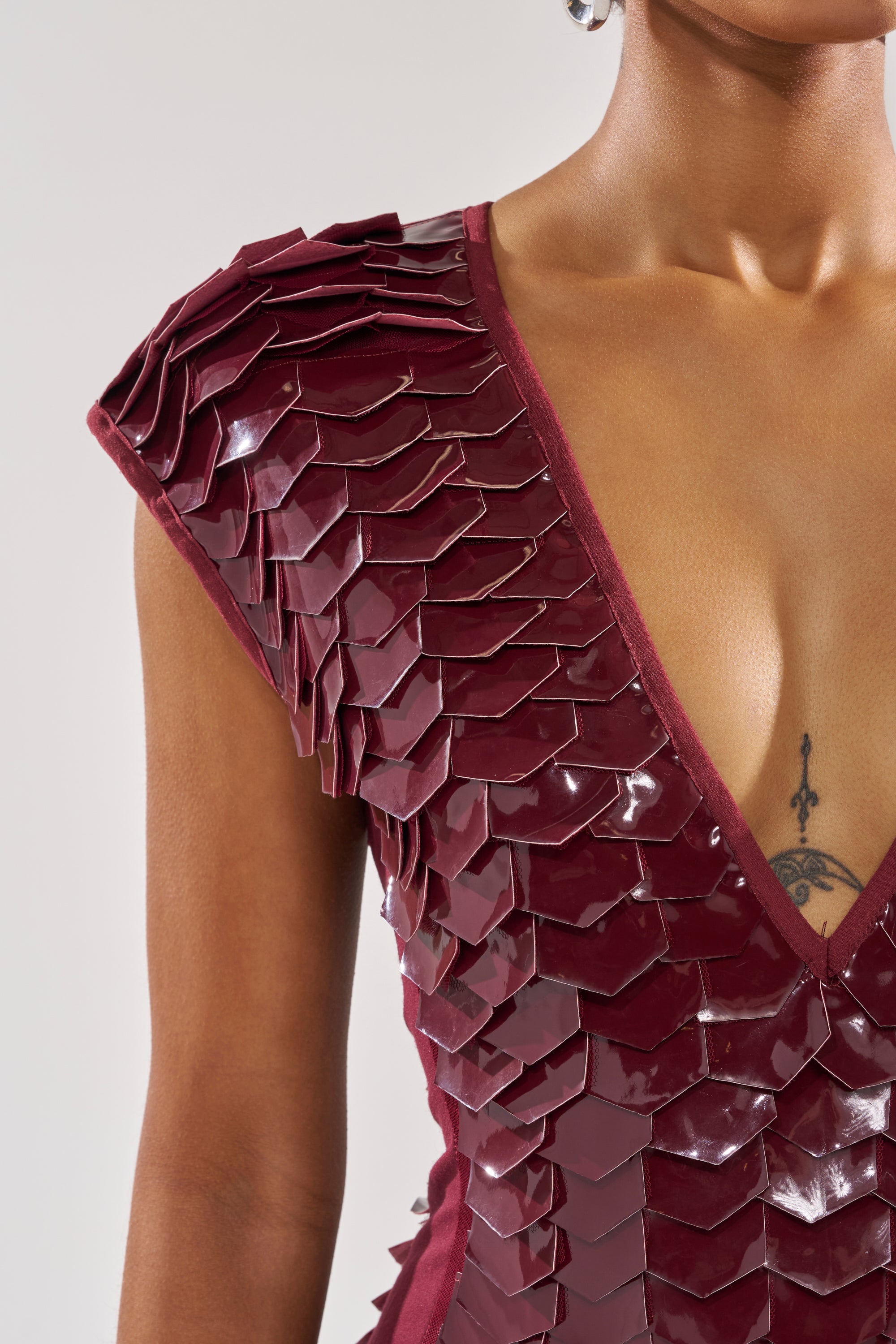 Wearing only the CRAZY IN LOVE SCALE MINI DRESS, this look features glossy burgundy scale-textured panels and a sleeveless deep V-neck design with an armor-inspired, futuristic style. Only the upper torso is shown.