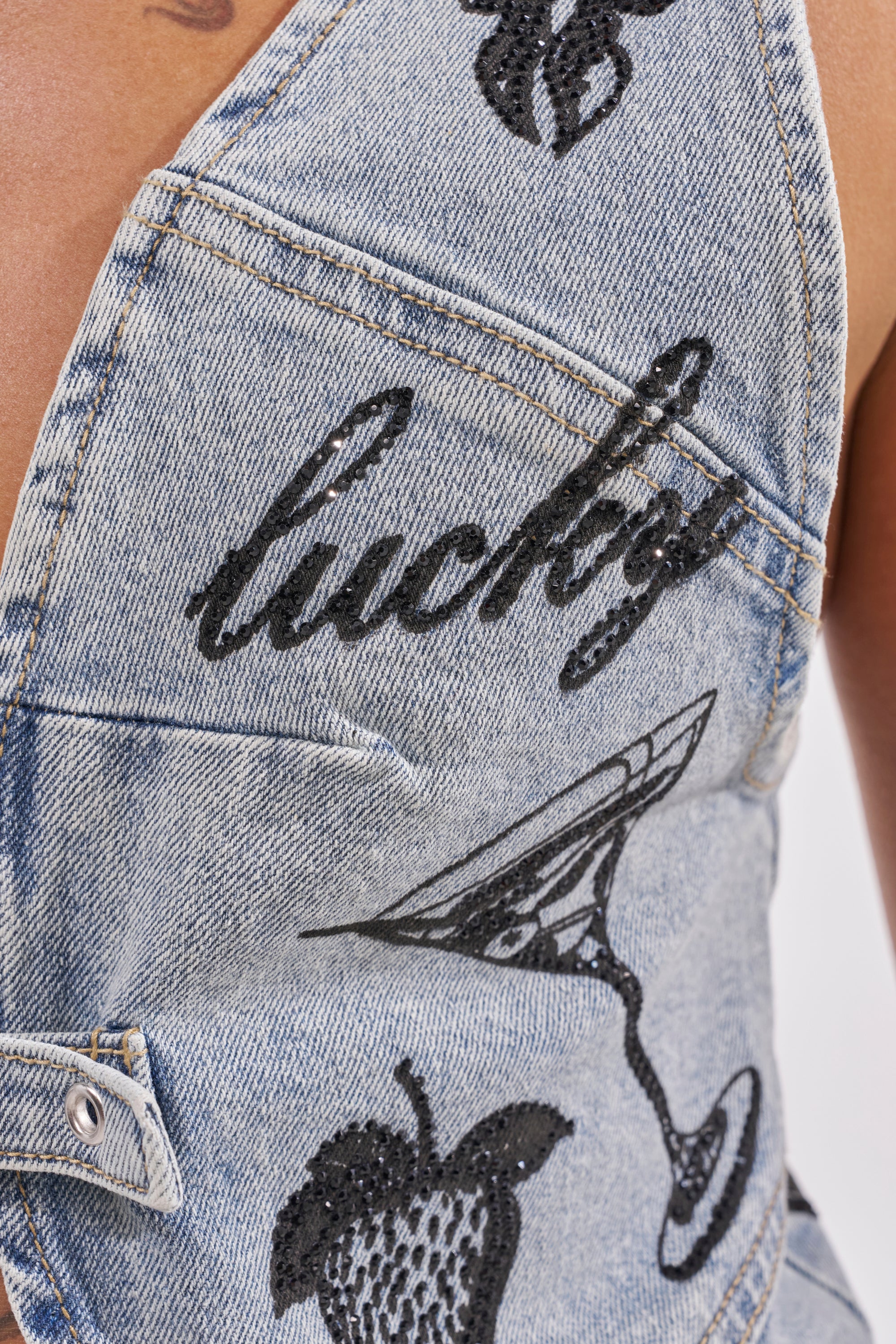 Close-up of the AFTER HOURS DENIM TOP, a Y2K-inspired cropped denim piece with black embroidery—"lucky," a martini glass, and strawberry. Features include visible stitching, button detail, and playful patterns for a nostalgic vibe. 7