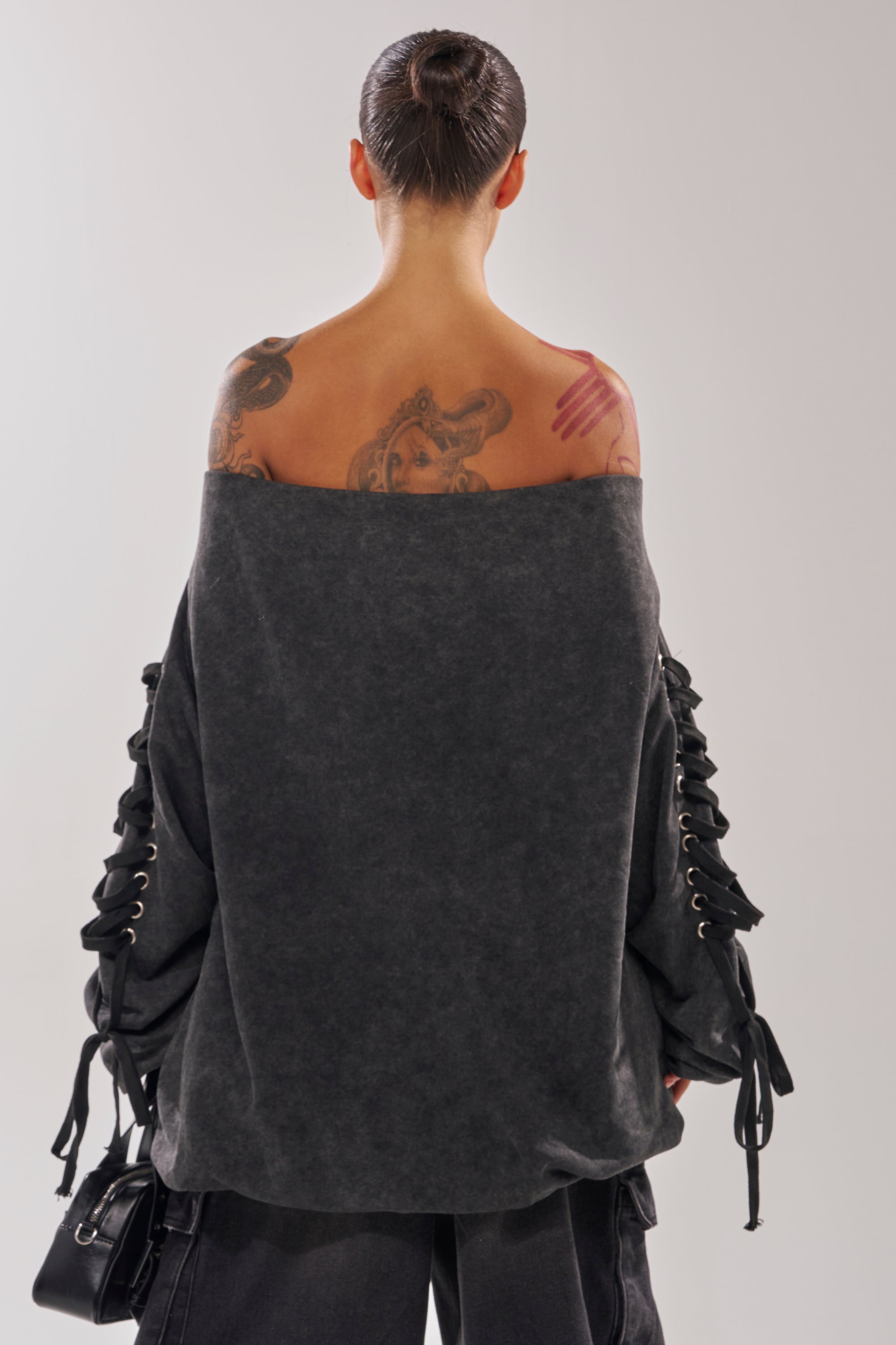A person with dark hair in a bun and visible tattoos is seen from behind, wearing the LACED UP FOR GOOD MINI DRESS, an off-the-shoulder mini dress with lace-up sleeve detailing.