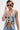 A confident individual with short, two-tone hair and tattoos wears sunglasses, a silver necklace, and the OUT OF MY LEAGUE DENIM HALTER TOP embroidered with flowers, a leopard, and yin-yang symbols.
