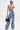 A person models the OUT OF MY LEAGUE DENIM HALTER TOP with matching light blue, wide-leg jeans. They accessorize with sunglasses, a black handbag, and a silver choker necklace.
