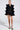 A person confidently poses against a plain background, wearing the LIVING OVER THE TOP RUFFLE SLEEVE BLAZER MINI DRESS with gold buttons, black and gold heels, and large statement earrings.