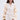 A woman with long brown hair models the LIVING OVER THE TOP RUFFLE SLEEVE BLAZER MINI DRESS, showcasing its sleek gold buttons and sheer ruffled sleeves. She holds a gold clutch and stands gracefully against a plain background.