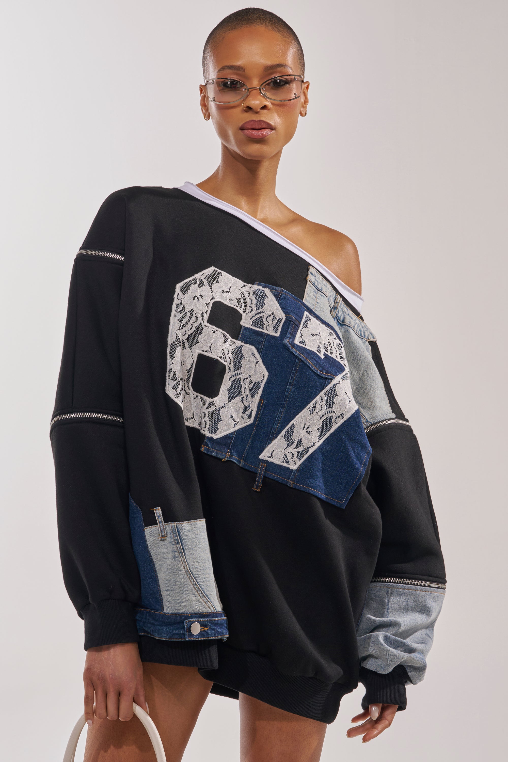 A stylish person in the DREAM TEAM FRENCH TERRY MINI DRESS with patchwork denim, lace accents, and a bold "67" on the front, sporting short hair, sunglasses, and carrying a white bag. 0