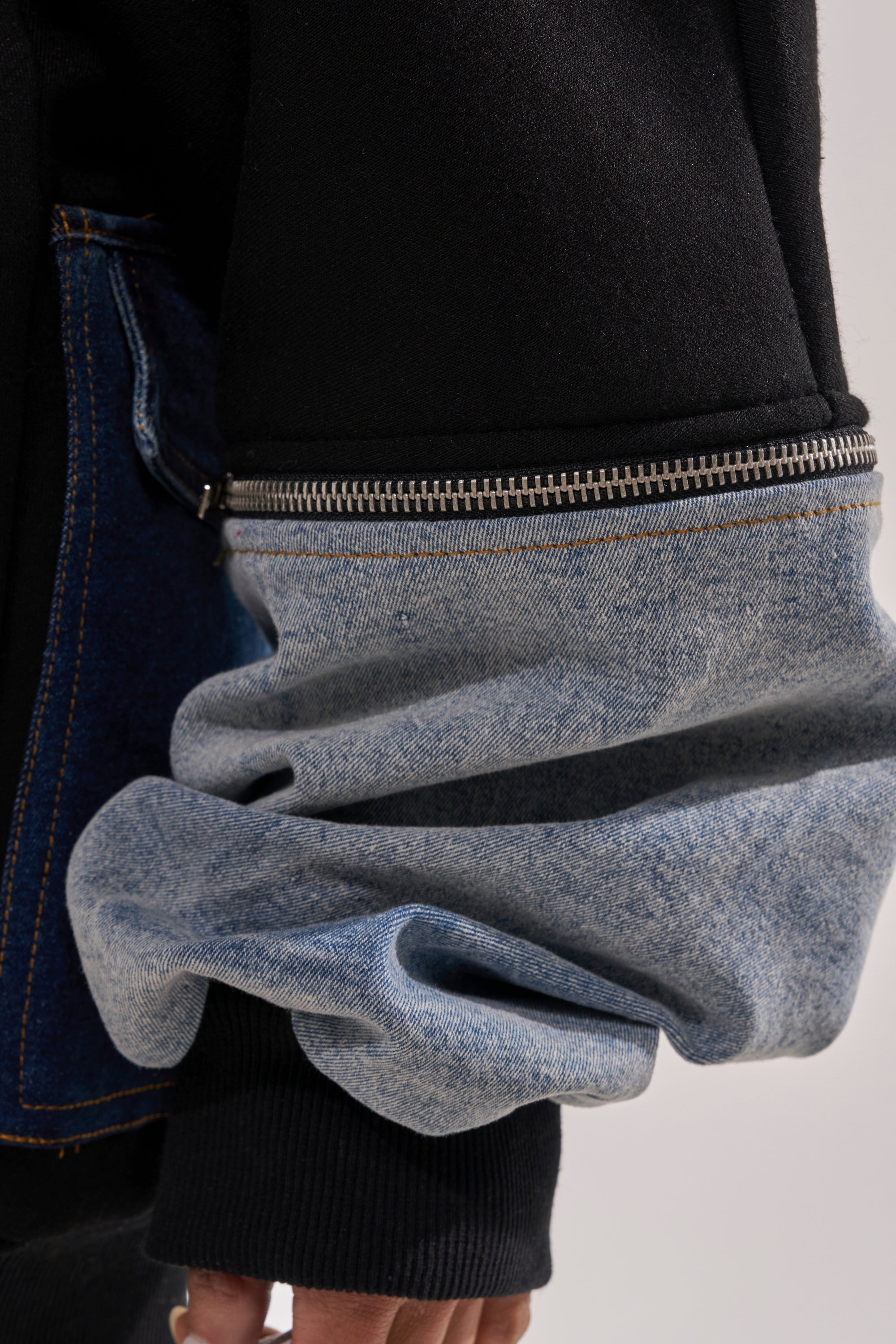 Close-up of a person’s arm in the DREAM TEAM FRENCH TERRY MINI DRESS, featuring a unique denim patchwork jacket with a black upper sleeve, blue denim lower sleeve, visible silver zipper, and scrunched denim at the wrist. 7