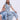 Two women exude cool style in light denim. One sits wearing a bow-accented shirt, while the other stands confidently in the COOL GIRL WIDE LEG DENIM JUMPSUIT and heeled sandals against a plain background.