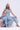 Two women exude cool style in light denim. One sits wearing a bow-accented shirt, while the other stands confidently in the COOL GIRL WIDE LEG DENIM JUMPSUIT and heeled sandals against a plain background.