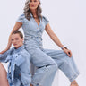 Two women exude cool style in light denim. One sits wearing a bow-accented shirt, while the other stands confidently in the COOL GIRL WIDE LEG DENIM JUMPSUIT and heeled sandals against a plain background.