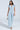 A person dons the COOL GIRL WIDE LEG DENIM JUMPSUIT with short sleeves and a button-down front, accessorized with a silver handbag and high-heeled sandals, set against a light gray backdrop.