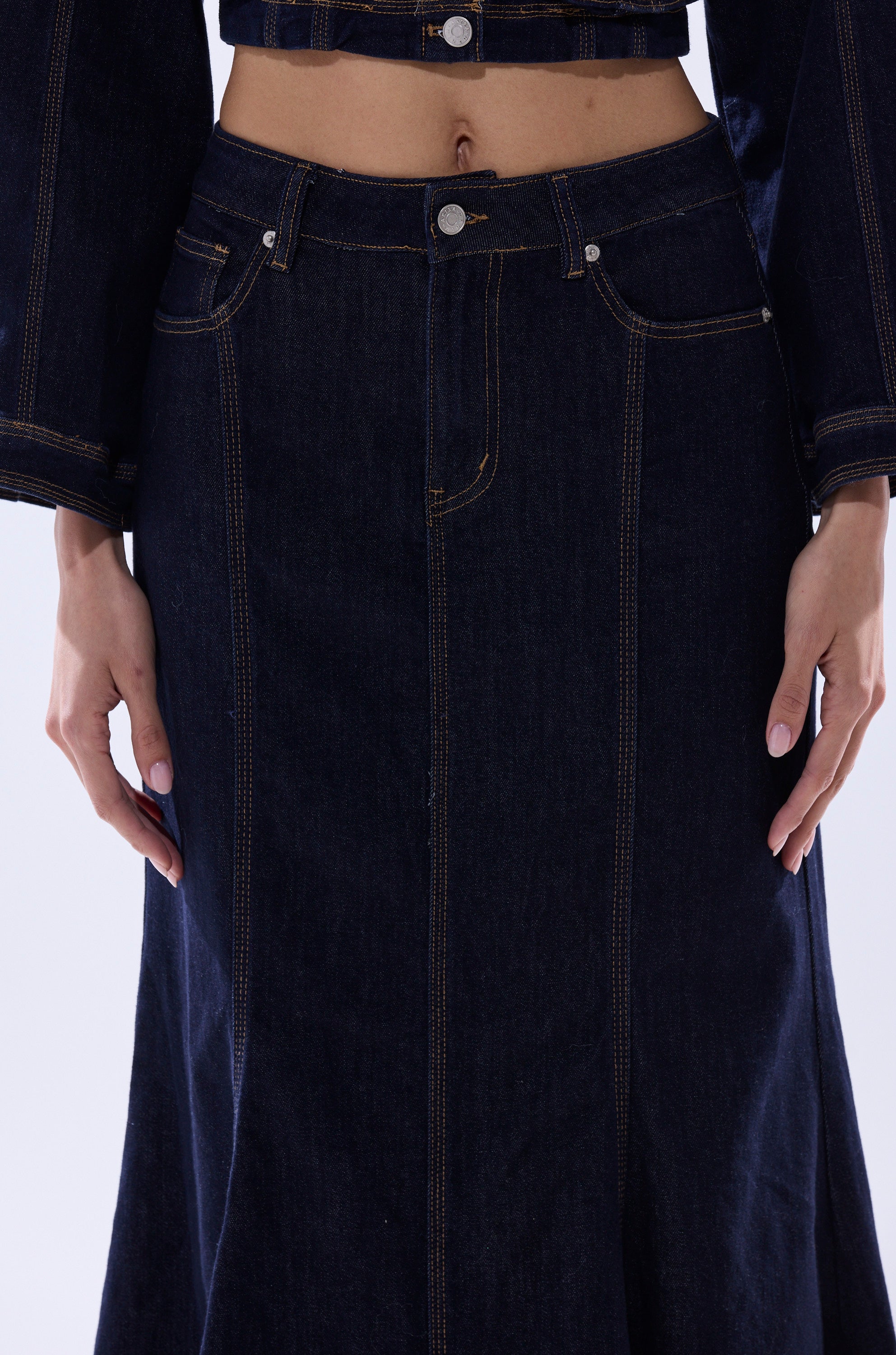 A person wears the SHES GONE, DANCE ON DENIM MAXI SKIRT with a matching denim jacket, hands at their sides. The photo is cropped from mid-torso to mid-thigh.