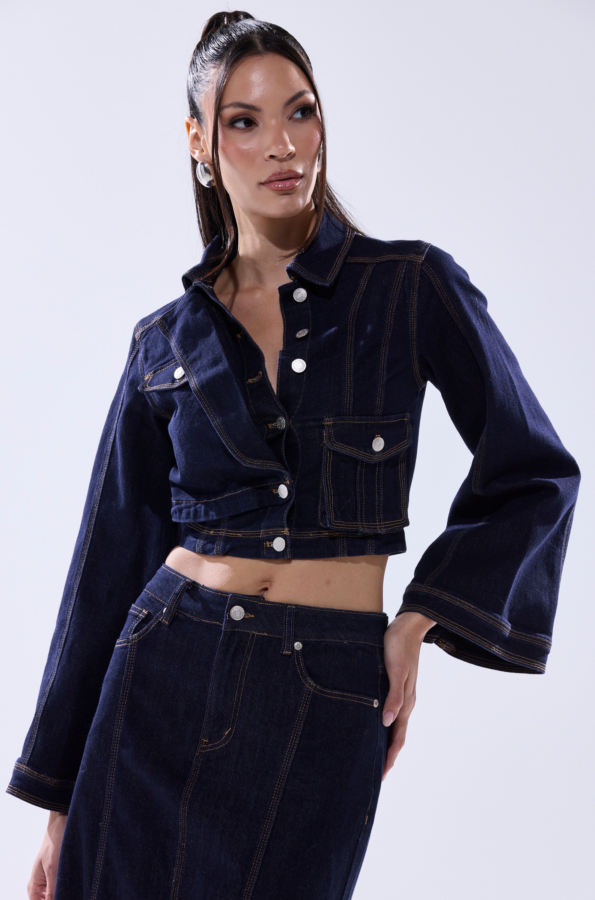 A woman poses for a picture wearing the SHES GONE DANCE ON DENIM BUTTON DOWN, styled as a cropped denim jacket over her shirt.