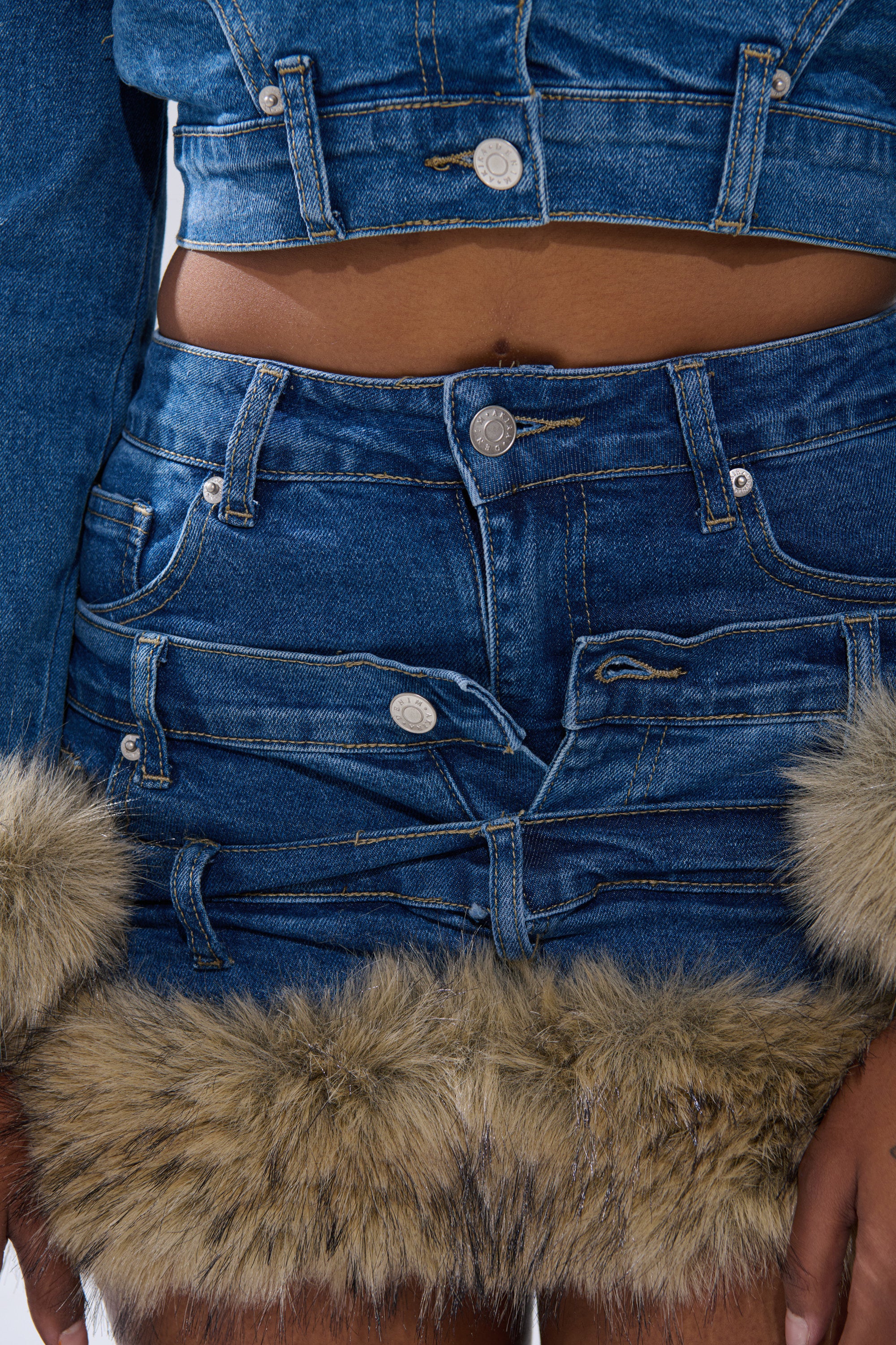 A close-up of a person wearing the FLUFFY DENIM MINI SKIRT and a matching blue cropped jacket with faux fur trim, multiple pockets, and silver buttons.
