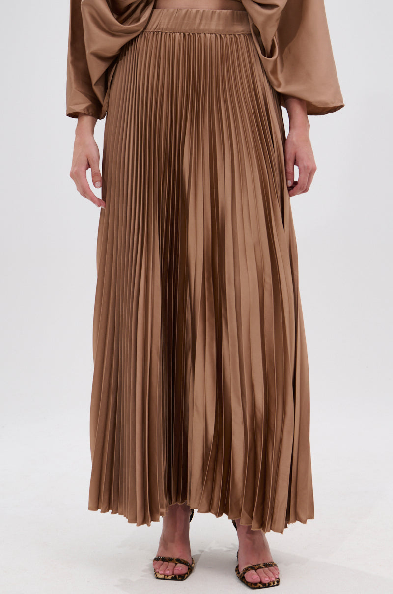 A person wears the MILLIE MOCHA MOUSSE SATIN MAXI SKIRT, showcasing a high-rise A-line cut with accordion pleats, styled with open-toe heels and arms relaxed at their sides against a simple backdrop. 1