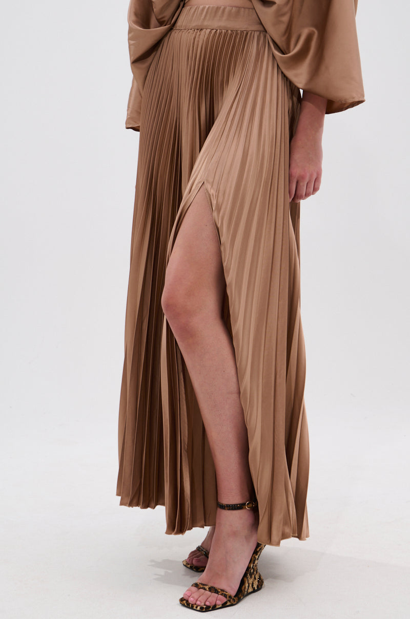 Wearing the MILLIE MOCHA MOUSSE SATIN MAXI SKIRT with accordion pleats and a high-rise A-line silhouette, paired with a matching top and animal print heels, a person poses against a plain white background. 2