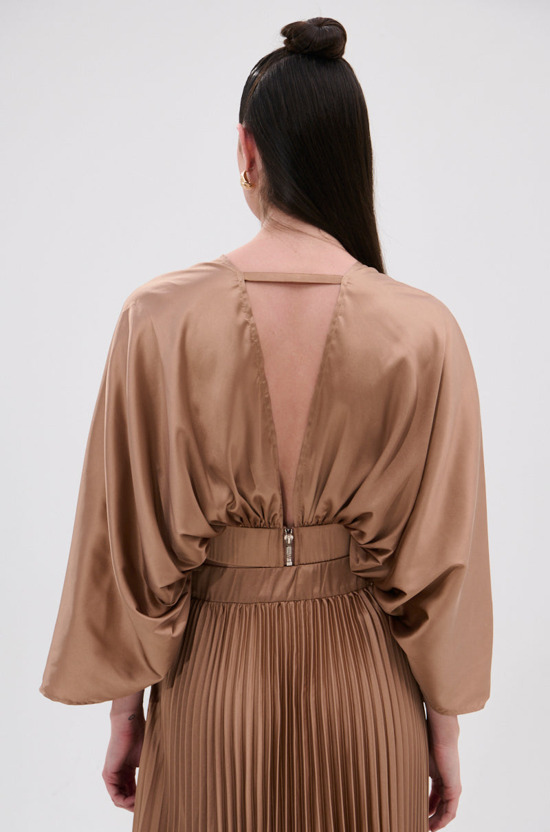 A woman with long dark hair in a top bun is seen from behind wearing the MILLIE MOCHA MOUSSE SATIN BLOUSE, featuring wide sleeves and a deep V-back with zipper closure in a shiny mocha hue. 3